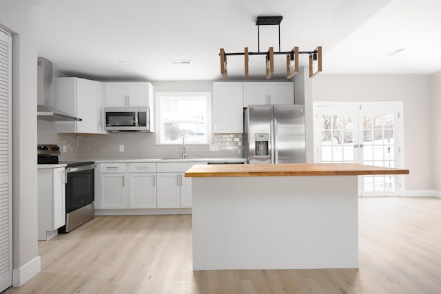 kitchen featuring appliances with stainless steel finishes, wall chimney range hood, and white cabinets