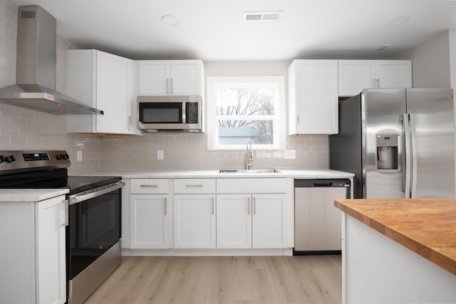 kitchen with white cabinets, appliances with stainless steel finishes, sink, and wall chimney range hood