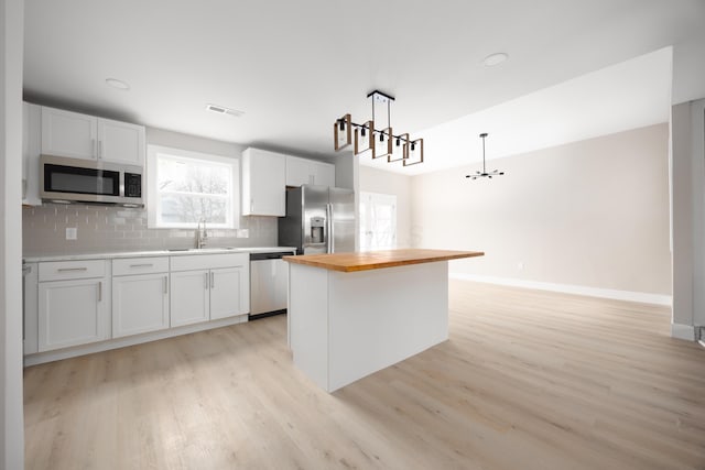 kitchen with a kitchen island, pendant lighting, white cabinetry, butcher block counters, and stainless steel appliances