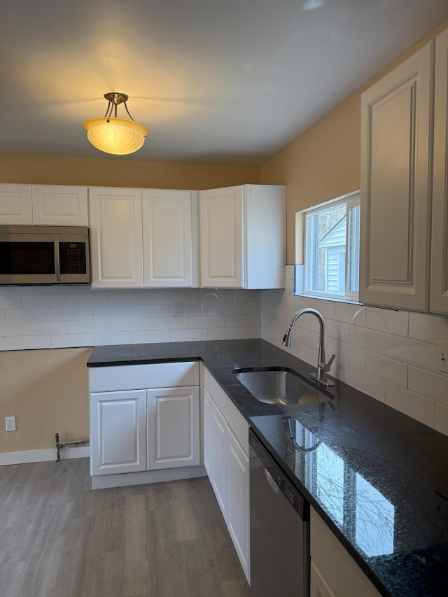 kitchen with appliances with stainless steel finishes, sink, dark stone counters, and white cabinets