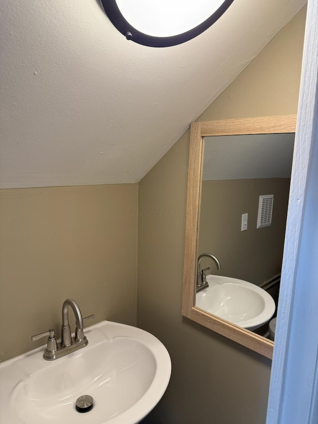 bathroom featuring sink, vaulted ceiling, and a textured ceiling