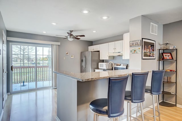 kitchen with appliances with stainless steel finishes, white cabinets, a kitchen breakfast bar, light stone counters, and kitchen peninsula