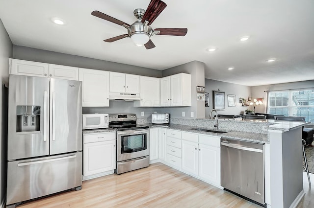 kitchen featuring white cabinetry, sink, kitchen peninsula, stainless steel appliances, and light stone countertops