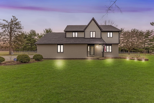 back house at dusk featuring a lawn