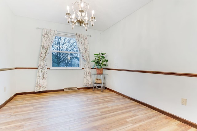 unfurnished room featuring an inviting chandelier and light wood-type flooring