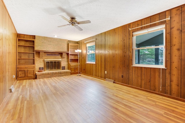 unfurnished living room featuring light wood-type flooring, built in features, a textured ceiling, and wood walls