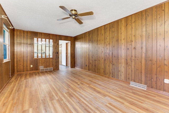 empty room featuring ceiling fan, light hardwood / wood-style flooring, and wood walls