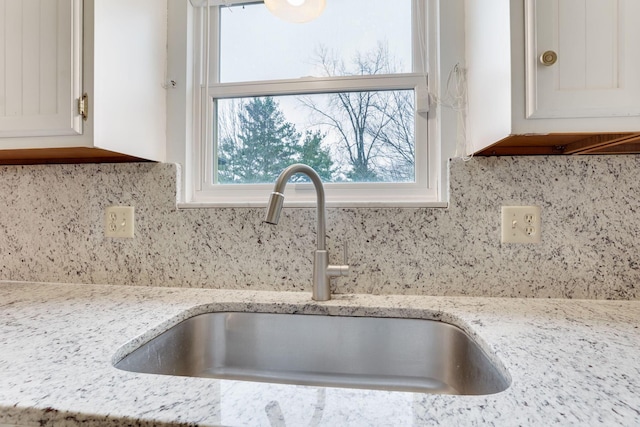 interior details featuring white cabinetry, sink, light stone counters, and decorative backsplash