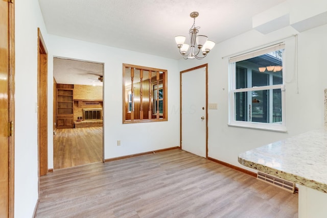 unfurnished dining area featuring an inviting chandelier, a fireplace, light hardwood / wood-style floors, and built in features