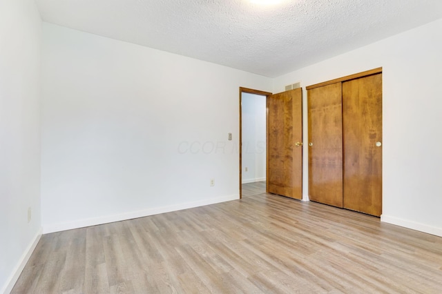 unfurnished bedroom featuring a textured ceiling, light wood-type flooring, and a closet