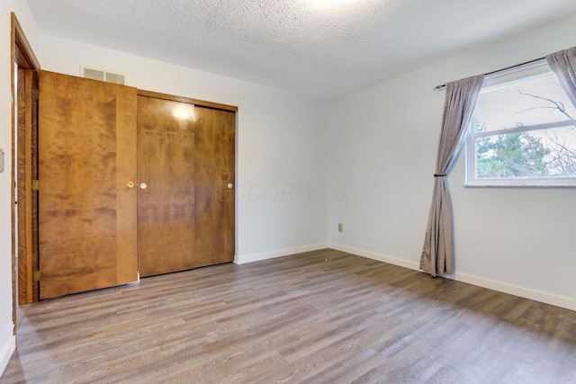 unfurnished bedroom with light hardwood / wood-style floors, a closet, and a textured ceiling