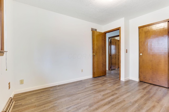 unfurnished bedroom featuring light hardwood / wood-style floors, a closet, a textured ceiling, and baseboard heating