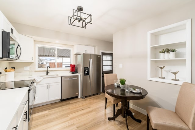 kitchen with appliances with stainless steel finishes, pendant lighting, white cabinetry, sink, and light hardwood / wood-style flooring