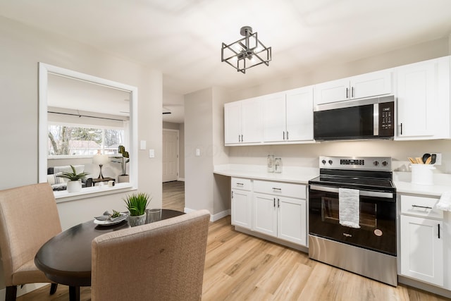 kitchen with a notable chandelier, stainless steel appliances, light wood-type flooring, and white cabinets