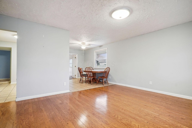 unfurnished dining area featuring ceiling fan, a textured ceiling, and light wood-type flooring