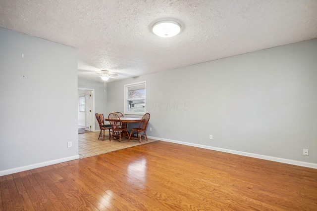 unfurnished dining area with ceiling fan, a textured ceiling, and light wood-type flooring