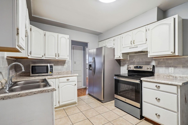 kitchen with light tile patterned flooring, appliances with stainless steel finishes, white cabinetry, sink, and decorative backsplash