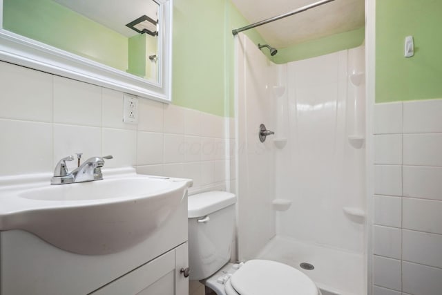 bathroom featuring vanity, a shower, tile walls, and toilet