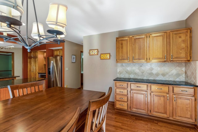 kitchen featuring pendant lighting, stainless steel fridge, backsplash, dark hardwood / wood-style flooring, and dark stone counters