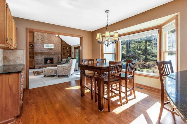 dining area with hardwood / wood-style flooring, lofted ceiling, a fireplace, and a notable chandelier