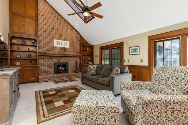 living room with ceiling fan, high vaulted ceiling, a brick fireplace, built in shelves, and light colored carpet