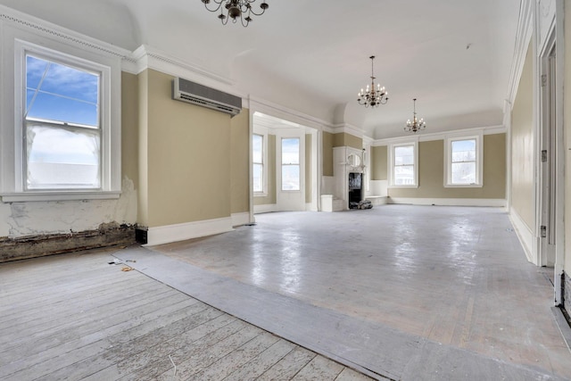 unfurnished living room with a notable chandelier, ornamental molding, a wall unit AC, and light wood-type flooring