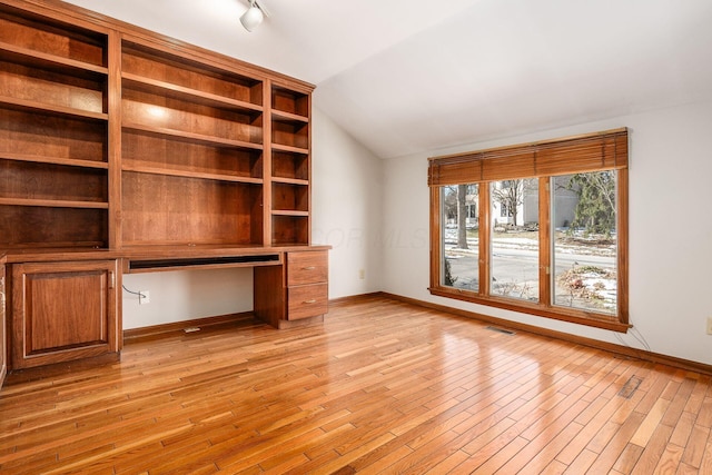 interior space featuring lofted ceiling, built in desk, and light hardwood / wood-style flooring