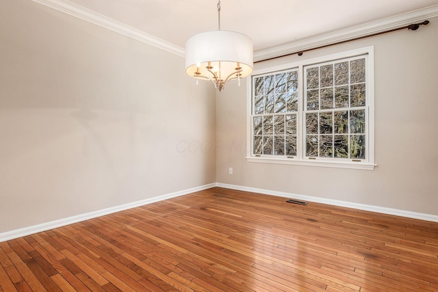 spare room featuring a notable chandelier, hardwood / wood-style flooring, and ornamental molding