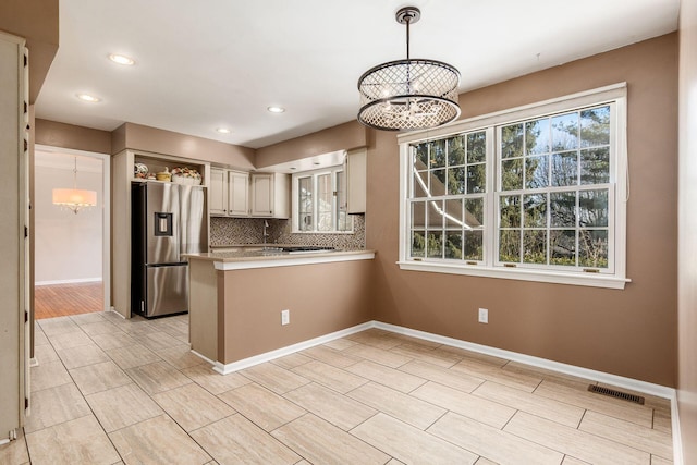 kitchen with pendant lighting, backsplash, stainless steel fridge with ice dispenser, kitchen peninsula, and a chandelier