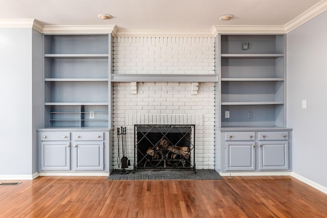 unfurnished living room featuring ornamental molding, wood-type flooring, a brick fireplace, and built in features