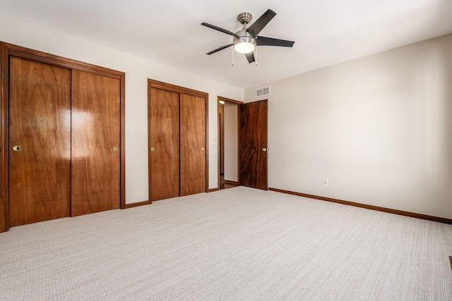 unfurnished bedroom featuring ceiling fan, multiple closets, and carpet