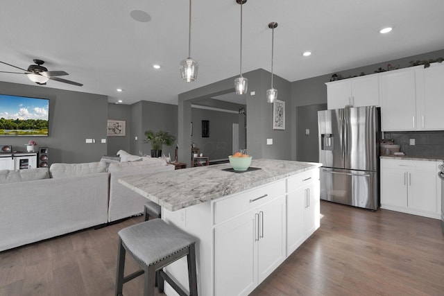 kitchen featuring white cabinets, light stone countertops, a center island, and stainless steel fridge