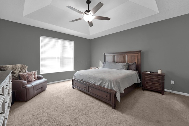 bedroom with light colored carpet, ceiling fan, and a tray ceiling