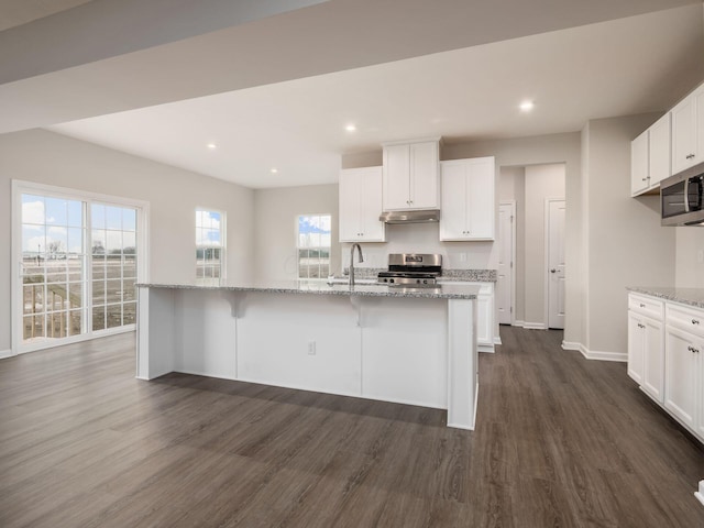 kitchen featuring white cabinetry, appliances with stainless steel finishes, light stone counters, and a center island with sink