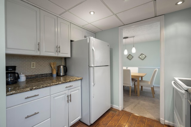 kitchen featuring white appliances, white cabinetry, tasteful backsplash, decorative light fixtures, and dark stone counters