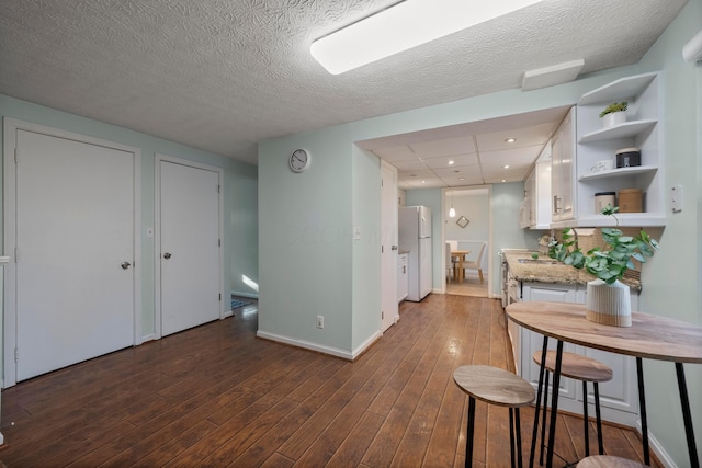 kitchen featuring a breakfast bar, white cabinets, dark hardwood / wood-style flooring, white fridge, and light stone counters