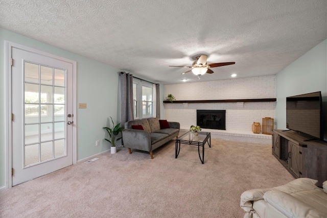 carpeted living room featuring ceiling fan, brick wall, a textured ceiling, and a fireplace