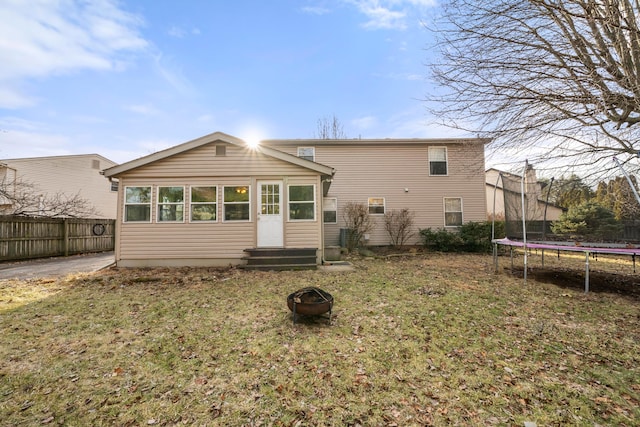 rear view of property with a fire pit, a trampoline, and a lawn