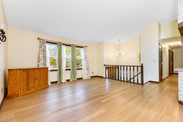 spare room featuring an inviting chandelier, light hardwood / wood-style flooring, and vaulted ceiling