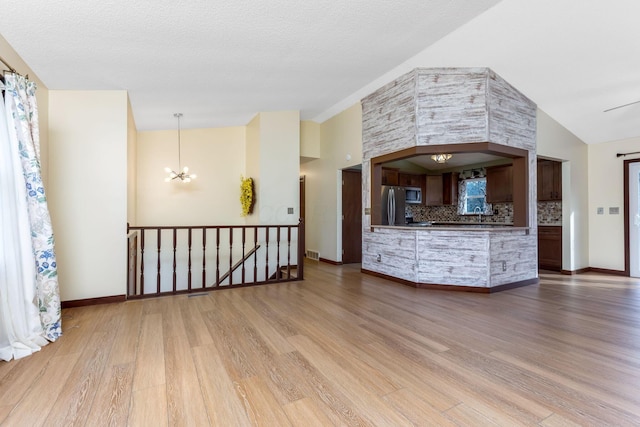 unfurnished living room featuring an inviting chandelier, high vaulted ceiling, and light hardwood / wood-style flooring