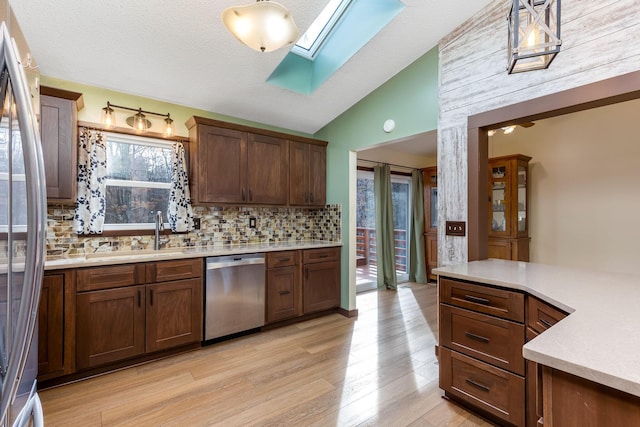 kitchen featuring sink, backsplash, lofted ceiling with skylight, stainless steel appliances, and light hardwood / wood-style floors