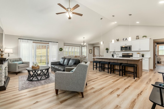 living room featuring sink, ceiling fan with notable chandelier, high vaulted ceiling, and light hardwood / wood-style flooring