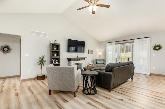 living room featuring ceiling fan, a stone fireplace, high vaulted ceiling, and light hardwood / wood-style floors