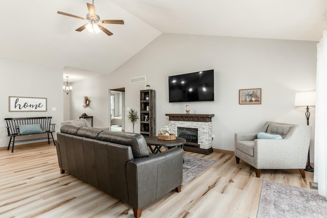 living room featuring lofted ceiling, ceiling fan with notable chandelier, a fireplace, and light wood-type flooring