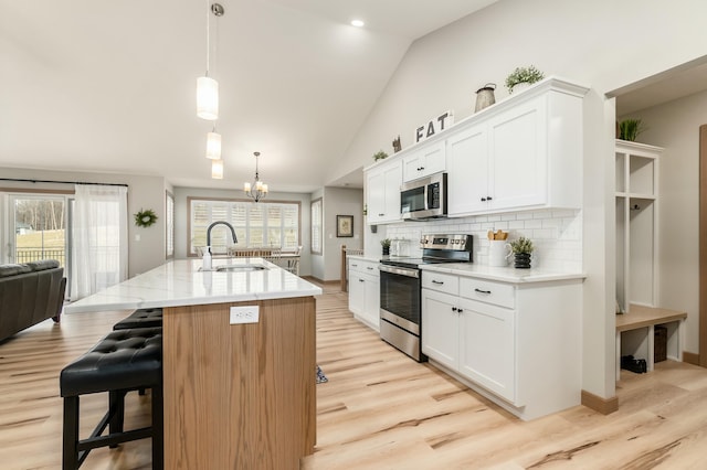 kitchen with stainless steel appliances, a kitchen island with sink, hanging light fixtures, and white cabinets