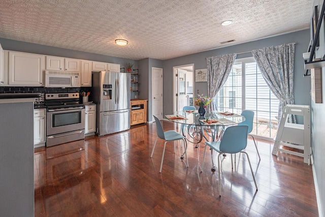 kitchen with stainless steel appliances, white cabinetry, tasteful backsplash, and dark hardwood / wood-style flooring