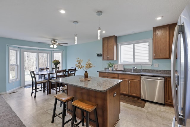 kitchen with a kitchen island, appliances with stainless steel finishes, pendant lighting, sink, and a kitchen bar