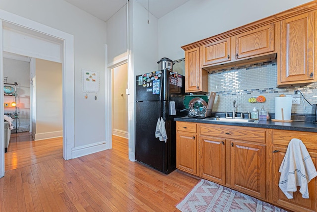 kitchen with sink, backsplash, light hardwood / wood-style floors, and black fridge