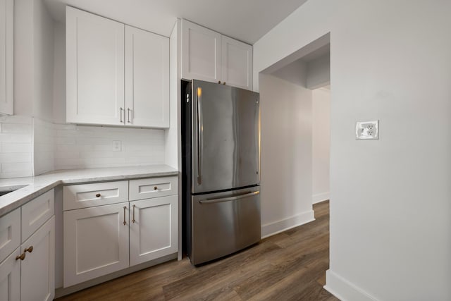 kitchen featuring dark hardwood / wood-style floors, stainless steel refrigerator, tasteful backsplash, white cabinets, and light stone counters