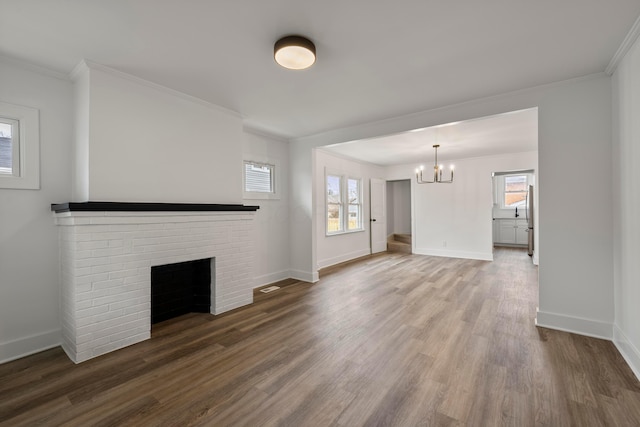 unfurnished living room with wood-type flooring, a brick fireplace, ornamental molding, and an inviting chandelier